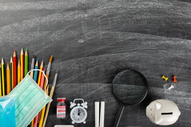 Okula dönmek ya da üniversite konseptine dönmek. Okul malzemeleri kırtasiye malzemesi ve ameliyat maskesinin karatahta arka planında görünümü güvenli eğitime dönüş salgın Coronavirüs salgını sırasında yeni bir normal.