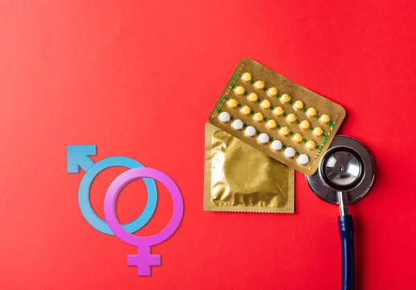 World sexual health or Aids day. Top view flat lay Male, female gender signs, condom in wrapper pack, birth control pill and doctor stethoscope on pink background, Safe sex reproductive health concept