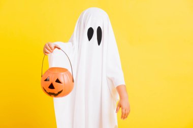 Komik cadılar bayramı çocuğu kavramı, beyaz kostümlü şirin çocuk Cadılar Bayramı hayaleti korkunç elinde turuncu kabak hayaleti, beyaz arka planda sarı bir stüdyo.