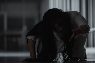 Korkunç kötü kadın hayalet sürünen sürüngen evdeki karanlık bir odada yavaşça sürünüyor. Kan içindeki dişi zombi korkunçtur. Terk edilmiş binaya dadandı. Mutlu Cadılar Bayramı festivali konsepti.