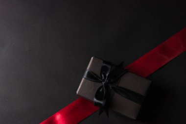 Kara Cuma İndirimi konsepti, hediye kutusunun üst görüntüsü siyah kağıt ve siyah kurdele presi, stüdyo çekimi ve arka planda kırmızı kurdele olması.
