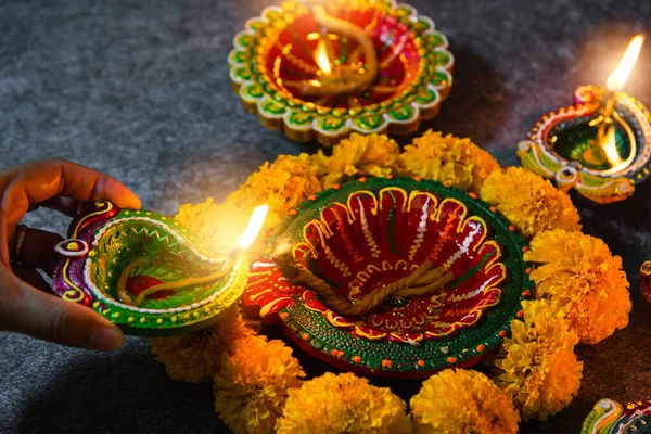 Close up woman hand being lit clay light fire on Diya or oil lamp studio shot on black wooden background, Decoration of Hinduism rangoli, Happy celebration Deepavali or Diwali festival concept