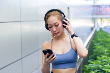 Egzersiz yapan kadın dışarıda spor yapıyor, kulaklıkları ayarlıyor, telefon ve akıllı kulaklıkları takip ediyor, düzenli egzersiz yaparak sağlık ve sağlık arayışında olan insanlar..