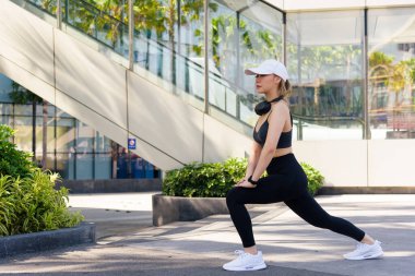 Spor kadını dışarıda egzersiz yapıyor, formda insanlar esneme hareketleri yapıyor, sağlıklı yaşam tarzını sürdürüyor, şehir ortamında spora büyük bir bağlılığı var..