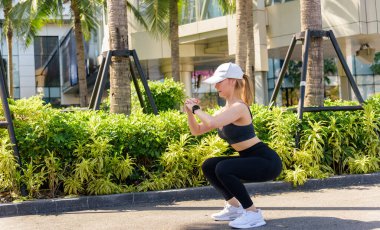 Spor kadını dışarıda egzersiz yapar, fit vücut derin çömelme egzersizi yapar, insanlar şehir sporunu sever, sağlıklı aktif yaşam tarzı esneme rutini de dahil..