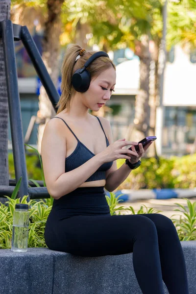 Antrenman yapan kadın açık havadan hoşlanıyor, genç formda spor modeli kulaklıkla telefonu kullanıyor, aktif egzersize hazırlanıyor, sağlıklı yaşam tarzı egzersizlerini benimsiyor..