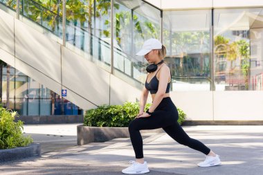 Egzersiz odaklı kadın spor meraklısı açık hava esneme hareketleri yapıyor, aktif fiziği yoğun antrenmanlara hazırlıyor, parlak güneş altında kentsel yaşam tarzının keyfini çıkarıyor..