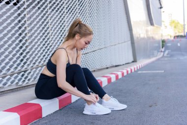 Egzersiz sporu yapan kadın spor ayakkabılarını dışarıda çalışmak için ayarlar, insanlar sağlıklı spor için vücut hazırlamaktan hoşlanırlar, hareketli egzersiz seanslarından önce ya da sonra esneme hareketleri yaparlar..