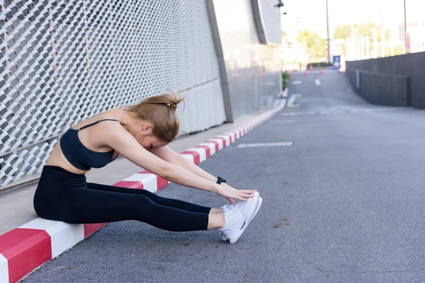 Antrenman yapan kadın açık hava spor egzersizleri yapıyor. Vücudu esneklik için esnetiyor. Kentsel sokak kaldırımında sağlıklı yaşam tarzı için modern binanın yanında faal egzersiz yapıyor..