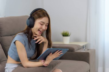 Genç kadın evde mutlu bir aktivite, dijital medyadan hoşlanan insanlar, müzik ya da podcast dinleyen, kulaklıkla tabletten videolar izleyen, kapalı alanda eğlenen.