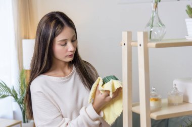 Temiz, genç bir kadın, evi temizliyor, yeşil yaprağı titizlikle sarı kumaşla siliyor, günlük temizlik işleriyle uğraşıyor, düzenli bir yaşam alanı sağlıyor..