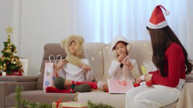 Mutlu bir aile Noel tatilini evde kutluyor, çocuklar rahat kış şapkaları takıyor süslü ağaçların yanında hediyeler açıyor, ebeveynler Noel Baba şapkası takıyor çocuklarla neşeli bir bayram sezonunun keyfini çıkarıyor..