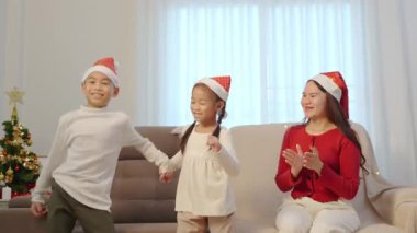 Mutlu aile Noel tatilini evde kutluyor, küçük çocuklar köpüklü ağacın yanında neşeyle dans ediyor, aileler el çırpıyor, neşeli bir gülümsemeyle şenlik sezonunun tadını çıkarıyorlar..