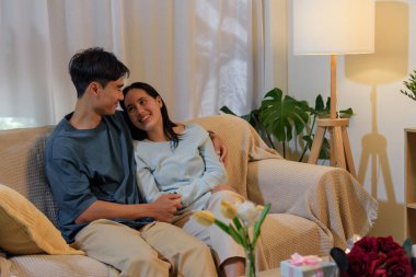 Mutlu genç çift evde aşkı paylaşıyor, erkek ve kadın romantik sevgililer gününün keyfini çıkarıyor, hoş bir akşam hediyelerle, çiçeklerle, yumuşak aydınlatmalarla, mükemmel bir özel ortam yaratıyor..