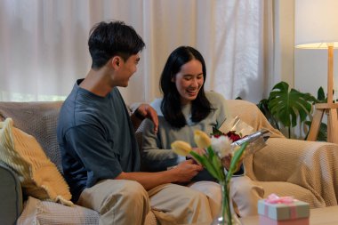 Mutlu genç çift evde sevişiyor, erkek kadına romantik sevgililer günü hediyesi veriyor, neşeli yıldönümü kutlaması için güller, derin bir sevgi ve saf zevk gösteriyor..