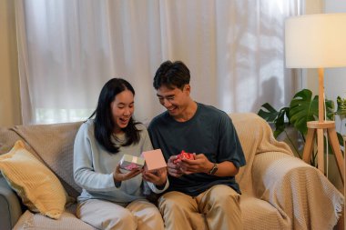 Mutlu genç çift aşklarını evde paylaşıyor, romantik sevgililer günü hediyelerini açıyor, büyük gülümsemeler ve neşeli ifadelerle anın tadını çıkarıyor..