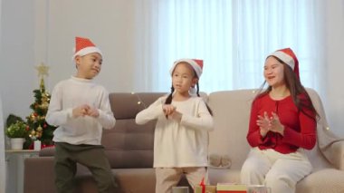 Mutlu bir aile Noel 'i evde kutluyor, iki neşeli çocuk aileleri için dans ediyor, Noel ağacı altında hediyeler, sıcak ışıklar rahat bir sahne oluşturuyor..