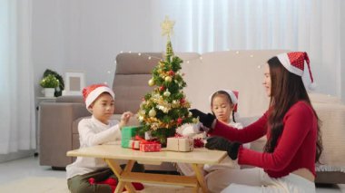 Mutlu bir aile Noel tatilini evde kutluyor, ebeveyn ve çocuk ağacı süslüyor, hediyeleri yerleştiriyor, bayram sezonunun tadını çıkarıyor, iç açıcı kış anıları yaratıyor..