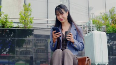 Genç, mutlu, modern ofis işkadını, dışarıda gezmekten hoşlanıyor, akıllı telefon, kahve fincanı, profesyonel seyahat için açık mavi valiz..