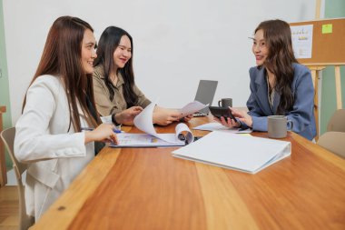 Yoğun kadınlar ofis işleri, takım pazar stratejisi, proje belgeleri ve hesaplamaları meşgul gülüşlü dizüstü bilgisayar ve hesap makinesi kullanarak gözden geçirmek için toplanıyor.