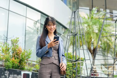 İş kadını, hayat tarzı seyahat, sokakta çalışan, gülümseyen, telefon kullanan, modern mimari ile şehir geçmişi olan, yeşil bitkiler canlı bir sahne yaratıyor..