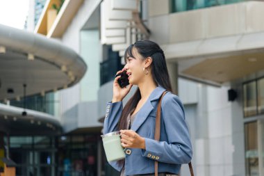 İş kadını telefonla konuşur, günlük iş seyahatleri için şehir sokaklarında dolaşır izole edilmiş içki bardağını tutar, şehir ortamında gezinen kendine güvenen kişi, modern mimari.
