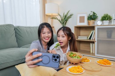 İki genç kadın taze salata ve lezzetli atıştırmalıklar yemekten hoşlanırlar. Arkadaşları telefonda selfie çekerken mutlu bir şekilde gülümserler..