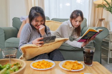 İki genç kadın gündelik boş vakitlerin tadını çıkarıyor, arkadaşlar çeşitli yemekler yiyor. Buna salata ve cips de dahil. Oturma odasındaki kanepede..