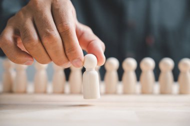 Beyaz ahşap bir figürü ahşap bir masanın üzerinde tutan bir el.. .