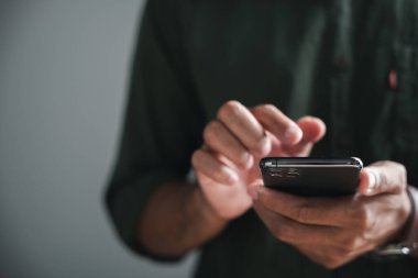 Akıllı telefonu tutan, parmakları ekrana dokunan bir insanın ellerinin yakın çekimi. Arka plan bulanık..