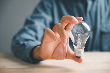Yakın plan erkek eli pozu ve elinde bir ampul olması ilham verici bir işaretti, umut verici bir işaret iş ve teknoloji için parlak bir fikri temsil ediyordu..