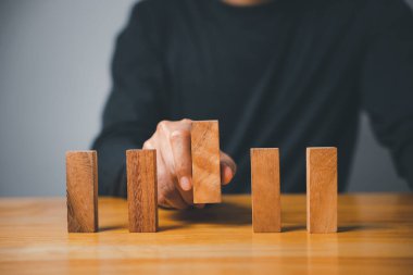 Bir el, tahta bir bloğu dört sıra halinde bir masanın üzerine koyar. Bloklar doğal ahşaptan yapılmış ve tahıl desenleri var. Masa hafif bir ağaçtan yapılmıştır.. .