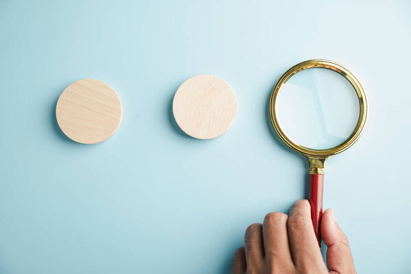 Sign of searching in this man hand pose and gesture closeup, he holds a magnifying glass over a blank wooden sign which is a symbol for finding the right business solution.