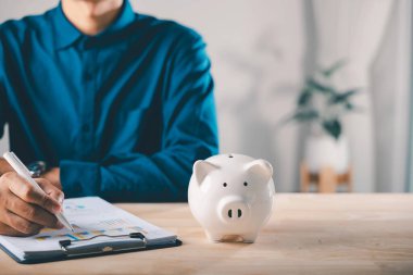 Piggy Bank finans para belgeleri kaydet yönetim çek belgesi, profesyonel kişi uzun vadeli mali istikrar için tahta masa üzerinde kalemle iş büyüme grafiklerini gözden geçiriyor.