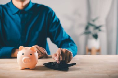 Adam vergi planı tasarrufu, emeklilik, mali yatırım konsepti, planlama, gelecekte tahta masada büyüyecek zenginlik için bütçe yönetimi için tasarruf yapmak için hesap makinesi ve domuz kumbarası parasını kullanıyor..