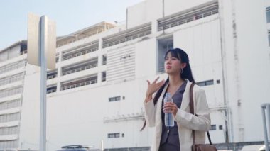 Sokakta yürüyen genç bir iş kadını, güneşten korunan gözler, su şişesi, modern ofis binalarına bakan şehir seyahati sırasında sıcak havaya dayanan profesyonel kariyer yolu..