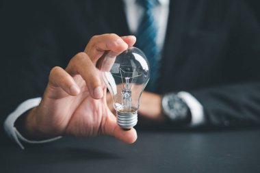 Ampulü tutan bir elin yakın çekimi, fikirleri ve çözümleri sembolize eder. Arka planda bulanık bir iş elbisesi.