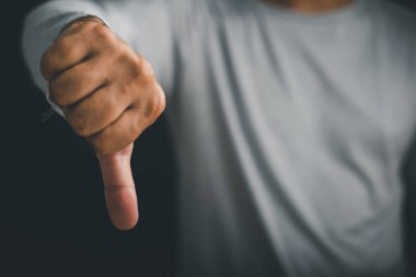 Bir adamın elinin yakın plan pozu, baş parmaklar aşağı işareti, hoşnutsuzluk gösteren bir jest ve açık bir anlaşmazlık işareti veya karanlık ve basit bir izole arkaplan üzerine olumsuz geri bildirim.