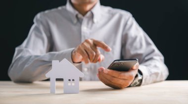 Arazi araması için akıllı telefon uygulaması kullanan kişi, gelecekteki yatırım planlama için ideal ev seçeneklerini dikkatlice düşünerek internette emlak listeleri buluyor.