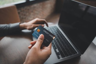 Yeni bir çağın işareti, bu adam el pozu ve jest yapıyor. Kredi kartı ve dizüstü bilgisayarla ödeme yaptığını gösteriyor. Güvenli online alışveriş ve e-ticaret aktivitesinin önemli bir işareti..