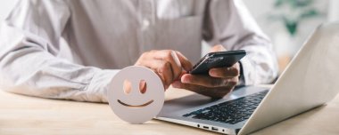 Çevrimiçi hizmet değerlendirmesi için olumlu müşteri memnuniyeti, mutlu müşteri değerlendirme konsepti, iş çalışanı telefon ve laptop kullanıyor, gülen yüz simgesi iyi kalite deneyimi gösteriyor.