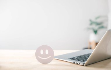 Mutsuz müşteri geribildirim analizi müşteri memnuniyetini, olumlu değerlendirmeyi ve iyi deneyimi, masadaki dizüstü bilgisayarın yanındaki mutlu yüz ifadelerini artırıyor..