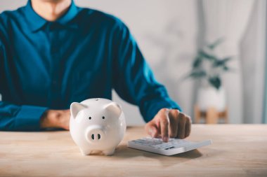 Vergi planı ve domuz kumbarasında tasarruf emeklilik için tasarruf, adam gelecek bütçe hedefleri ve zenginlik büyümesi yönetmek için hesap makinesi ile finansal planlama ve yatırım kavramı kullanır.