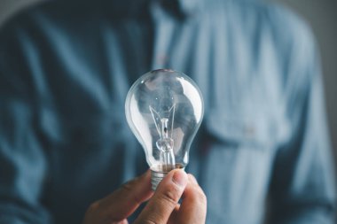 Bulanık mavi arka planda ampulü tutan bir elin yakın çekimi. Fikir, yenilik, ilham