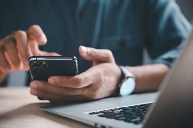 Dizüstü bilgisayar klavyesinin üzerinde kameralı mercekli akıllı telefonu tutan ellerin yakın çekimi.