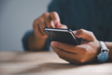 Kol saati ve arka planda ahşap bir masa olan akıllı bir telefonu tutan birinin ellerinin yakın plan fotoğrafı..