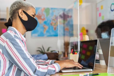 Yaratıcı ortamda çalışan gençler cerrahi maske takıyor ve Corona virüsünün yayılmasını önlemek için sosyal mesafeyi koruyorlar.