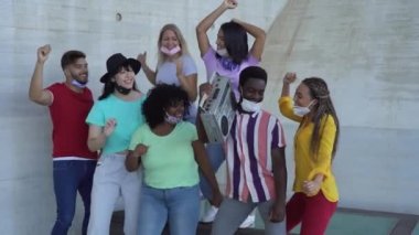 Mutlu arkadaşlar maske takıp dışarıda klasik müzik dinliyorlar, çok ırklı gençler Corona virüsü salgını sırasında birlikte dans ediyorlar.