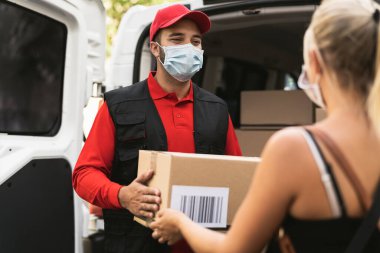Corona virüsünün yayılmasını önlemek için maske takan teslimatçı genç bir kadın Kurye Express 'ten online sipariş paketi alıyor.