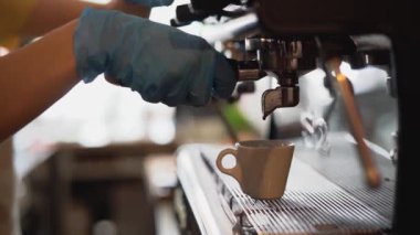Corona virüsünün yayılmasını önlemek için ameliyat eldiveni giyerek kahve yapan genç bir kadın.